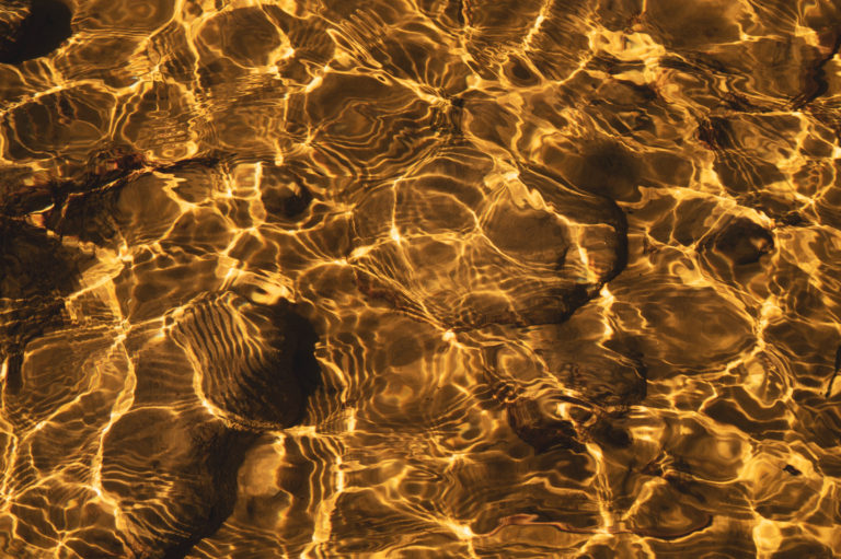 Shiny transparent water. clear water with pebbles and stone on the bottom. shining reflections of sun rays and ripples on the water surface